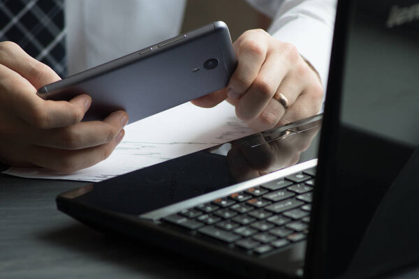 Business man drinking coffee and using laptop computer and mobile smart phone at home, young man browsing internet on phone, e commerce or online working from home, IOT internet of things concept.