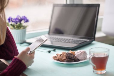 Pazar sabahı kafede içki içen ve cep telefonu kullanan genç bir kadın.