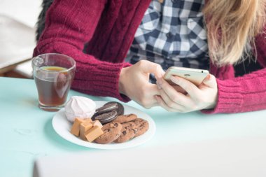 Pazar sabahı kafede içki içen ve cep telefonu kullanan genç bir kadın.