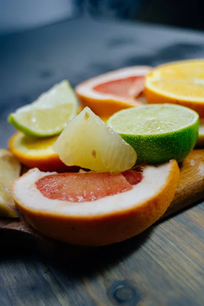 Various citrus fruit cut into slices orange, lemon, lime, grapefruit, pomelo. Spread out on a wooden board on a vintage background of natural wood texturing.