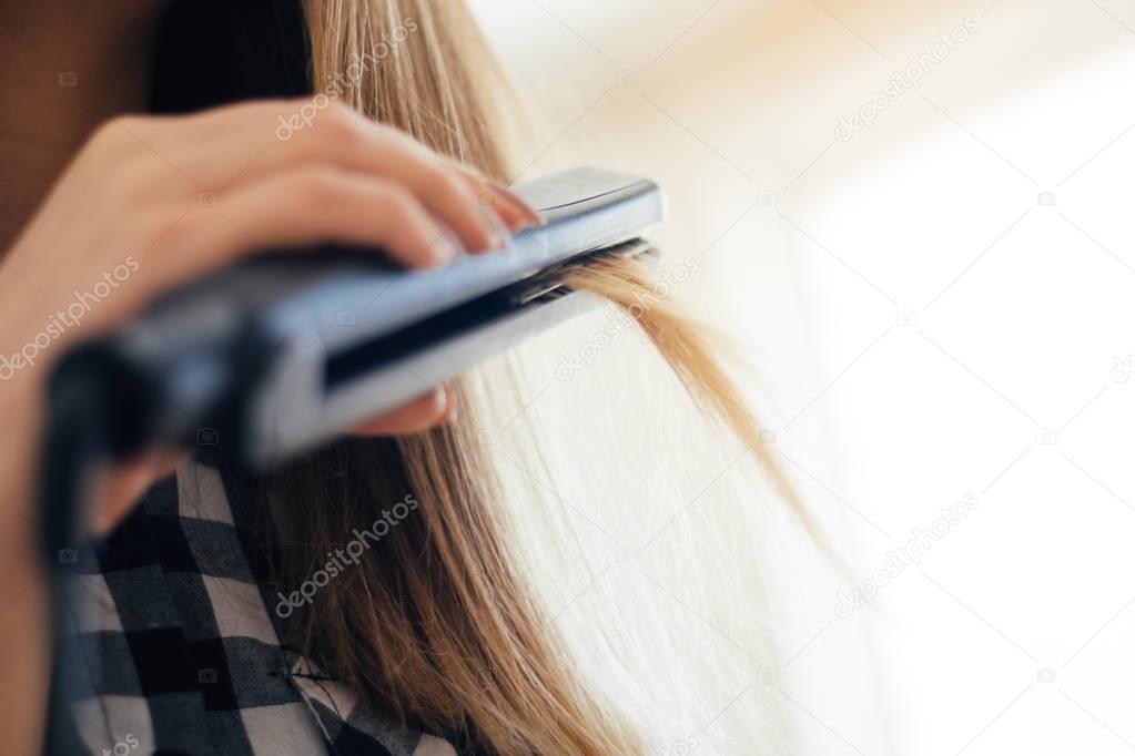 Woman doing hairstyle with hair straightener