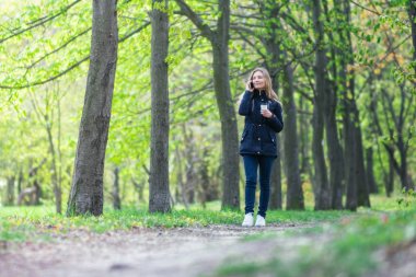 Evet, bir kız sabah bir smartphone ve kahve ile bir parkta yürüyor