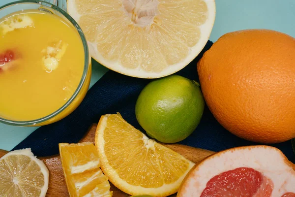 Citrus, oranges, lemons, limes, grapefruit, pomelo on vintage board, lemonade and juice in a glass of glass on a turquoise background