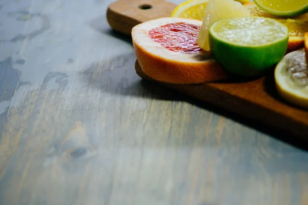 Varios cítricos cortados en rodajas naranja, limón, lima, pomelo. Extiende sobre una tabla de madera sobre un fondo vintage de textura de madera natural . — Foto de Stock