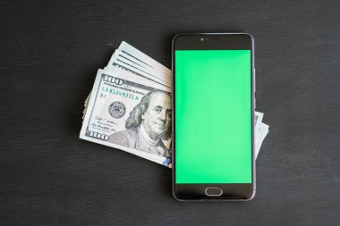 Smartphone ile chromakey anahtarlama ve bir siyah mockup için yüz dolar banknotlar ABD ile ahşap masa dokulu. Yeni Finans teknolojileri ve iş haberleri kavramları. Yatay