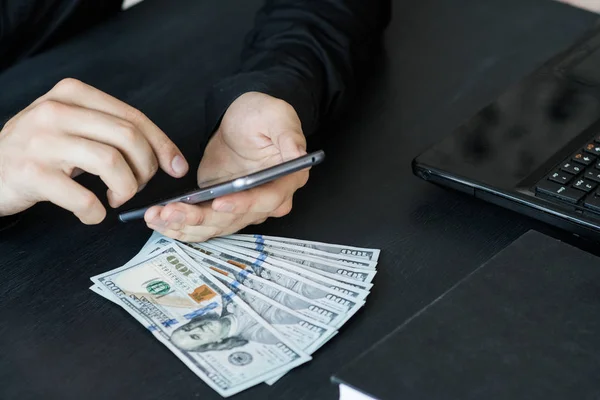 Technology, online banking, money transfer, e-commerce concept. Businessman using smartphone dollar bills flying on grey wall background. Internet earnings concept