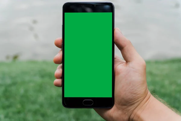 close-up hand of man holding mobile smart phone with chroma key green screen on gren background