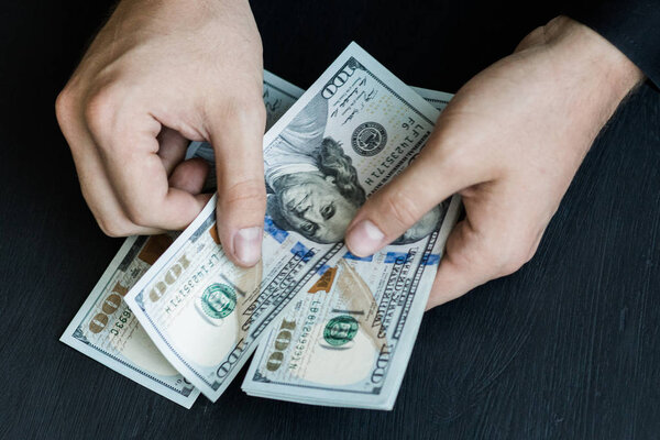 The white young man counts the money, one hundred new dollar bills on a black background close plan. Concepts of business and finance. top view .