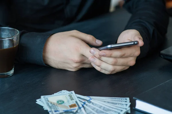 Technology, online banking, money transfer, e-commerce concept. Businessman using smartphone dollar bills flying on grey wall background. Internet earnings concept