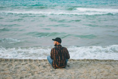 Okyanus arka planı şafakta oturan bir genç beyaz turist adam. Turizm ve yaşam tarzı kavramları