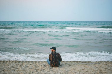 Okyanus arka planı şafakta oturan bir genç beyaz turist adam. Turizm ve yaşam tarzı kavramları