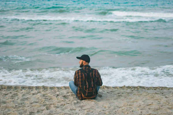 Okyanus arka planı şafakta oturan bir genç beyaz turist adam. Turizm ve yaşam tarzı kavramları