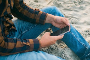 Tatlı adam turist kumlu plaj arka plan üzerinde hareket eden smartphone kullanarak. Çevrimiçi bağlantı, iletişim mesajlaşma, bankacılık için fotoğraf konsepti..