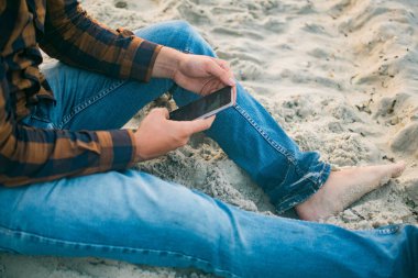 Tatlı adam turist kumlu plaj arka plan üzerinde hareket eden smartphone kullanarak. Çevrimiçi bağlantı, iletişim mesajlaşma, bankacılık için fotoğraf konsepti..