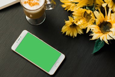 siyah ahşap bir yeşil ekran yeşil ekran, chroma anahtar yeşil dağ eteğindeki taş yığını ve ayçiçeği kitap ve latte dinlenme kavramı ile mobil akıllı telefon smartphone 