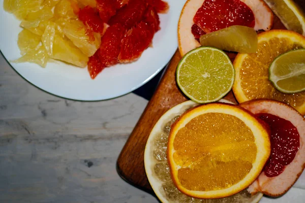 다양 한 감귤 류 과일 슬라이스 오렌지, 레몬, 라임, 자 몽, 포 멜로 오렌지 주스의 유리를 잘라. 나무 보드와 천연 나무의 배경에 빈티지 화이트 접시에 밖으로 확산 — 스톡 사진