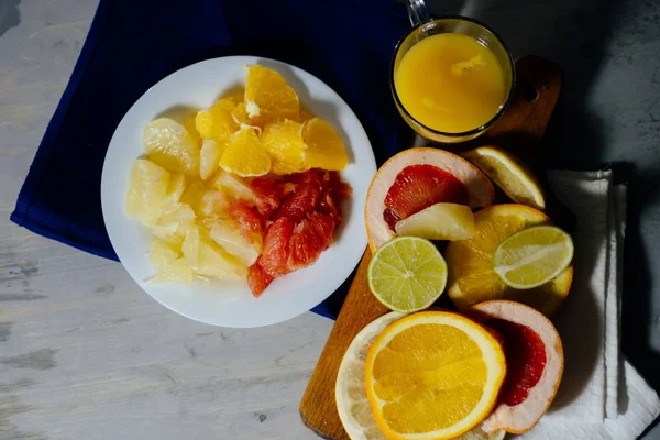 Diverse citrusvruchten snijd in plakjes oranje, citroen, limoen, grapefruit, pomelo en een glas jus d'orange. Verspreid op een houten plank en een vintage witte plaat — Stockfoto