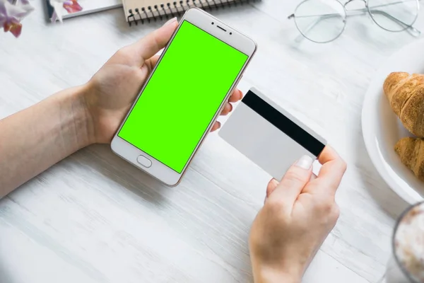 Smartphone and credit debit card in the hands of the girl smartphone green screen for chroma key. Internet commerce and payments for goods and services via the Internet for online shopping