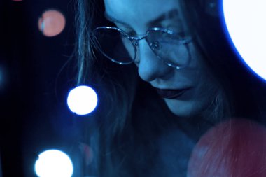 Karanlık ve bokeh mavi renklendirme güzel beyaz kızla gözlük bir moda portre. Netlik düşük yoğunluklu odak etkisini.