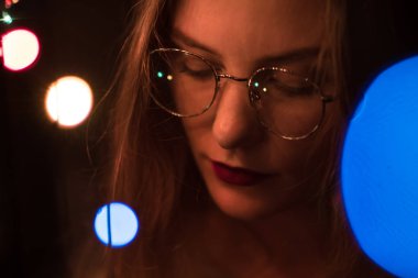Karanlık ve turuncu renklendirme bokeh güzel beyaz kızla gözlük bir moda portre. Netlik düşük yoğunluklu odak etkisini.