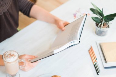 Bir kitap okuma ve fincan çay ya da kahve tutan genç kadın. Tonlu görüntü