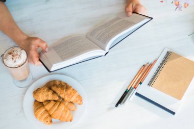 Bir kadın açma ve ahşap masa vintage kafede kahve fincanı ile bir kitap okuma