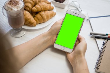 bir kafede yeşil ekran, chroma anahtar yeşil ekran beyaz arka planda, yeni teknoloji kavramı ile akıllı telefon elinde Smartphone