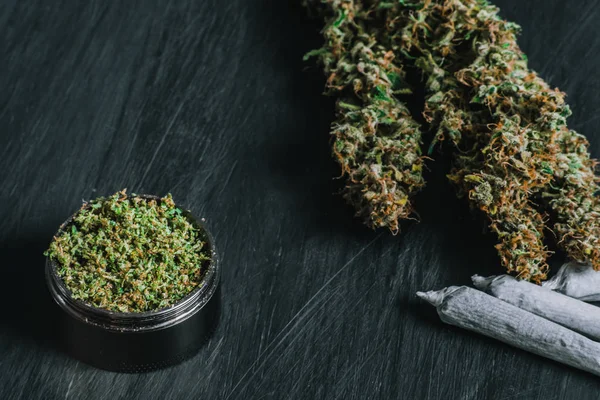 Macro van marihuana met schubben en geplette onkruid en warmgewalste joint in een slijper voor het hakken van een canapis op een zwarte lijst — Stockfoto