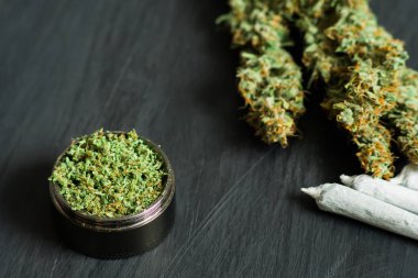 Makro esrar trichomes ve ezilmiş ot ve haddelenmiş ortak bir canapis siyah bir masada doğramak bir değirmeni