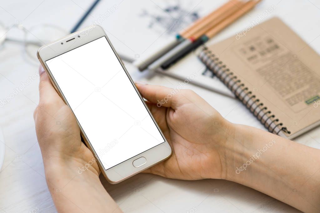 mock up of smart phone in girls hands In a cafe on the background of a wooden white table close up Phone with a white screen