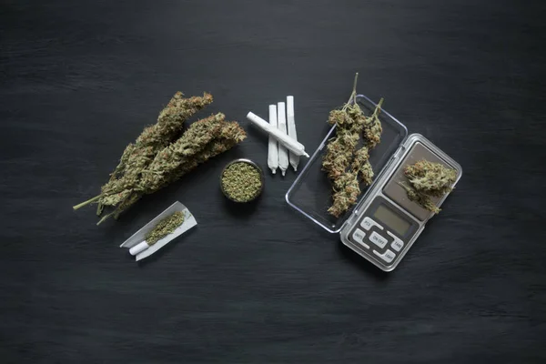 Marijuana, scales, jambs and a cannabis grinder weed on a black wooden table top top view — Stock Photo, Image
