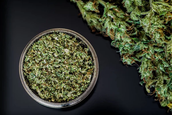 Macinino con erba schiacciata cannabis, germogli di marijuana, su sfondo nero macro vista dall'alto — Foto Stock