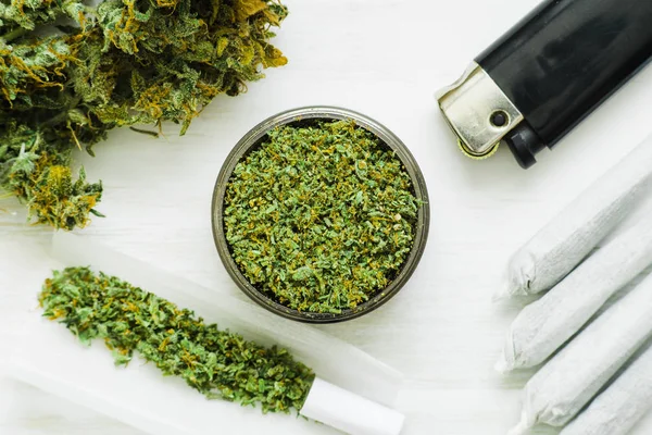 Joint and a grinder with crushed weed Leaf of cannabis, buds of marijuana, unrolled weed on a white wooden background top view — Stock Photo, Image
