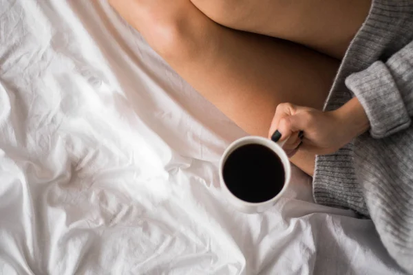Kvinnan avslappnande på mysiga hem atmosfär på sängen. Ung kvinna med med kopp cofe eller kaffe i hennes händer njuter av komfort. Mjukt ljus och bekväma skönhet Naturlig livsstil. Kopiera utrymme ovanifrån — Stockfoto