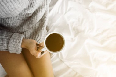kız yatakta fincan kahve kopya alanı üst tutan yün kazak giyen görüntülemek sarı ışık renklendirme