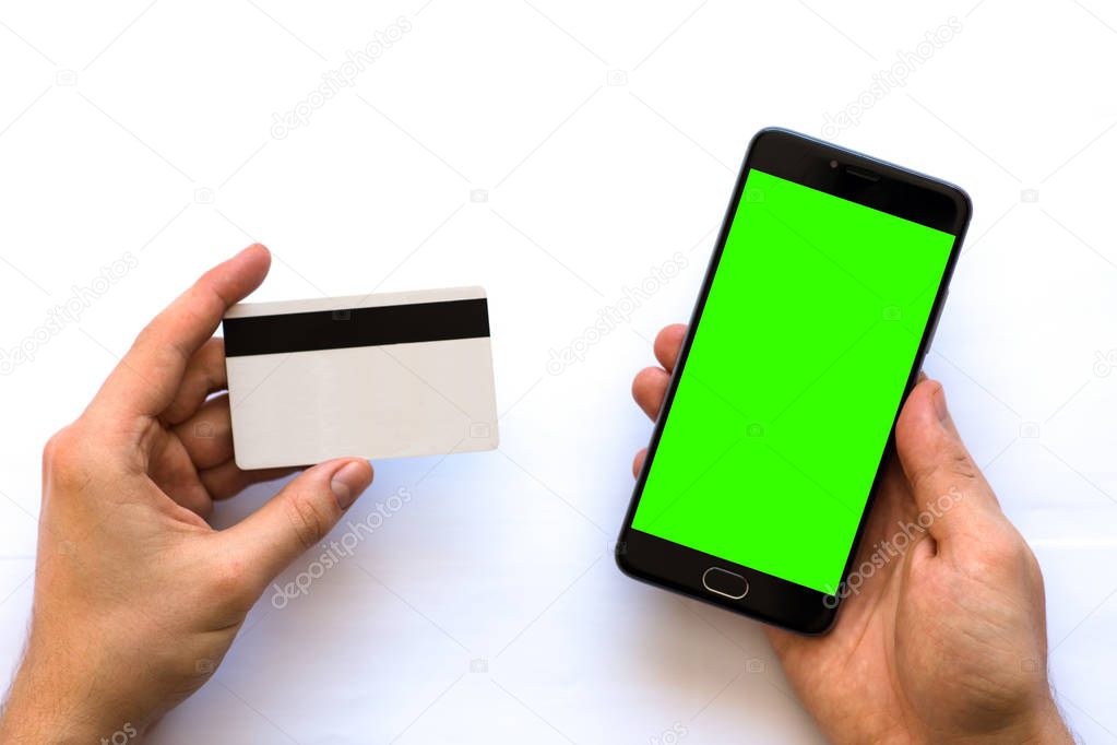 Smartphone with green screen for chroma key compositing and a credit card in the hands of a man on a white background, Internet commerce of online banking to pays in Internet, top view. isolated