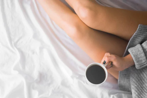 Chica en la cama con suéter de lana que sostiene la taza de espacio de copia de café vista superior Tintado de luz blanca —  Fotos de Stock