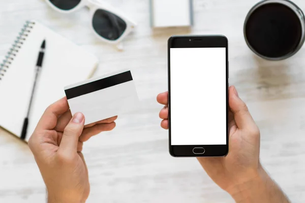 A black smartphone mock up and a credit card in the hands of a man on a rural white background, concepts of Internet commerce and the use of online banking to pay