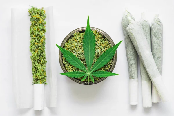 Giunto e un tritacarne con erba schiacciata Foglia di cannabis, marijuana, erba srotolata su uno sfondo bianco vista dall'alto da vicino — Foto Stock