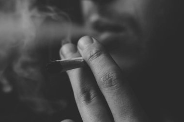 Siyah bir arka plan üzerinde duman. Bir adam sigara esrar esrar, esrar ve çakmak elinde. Tıbbi esrar kullanım ve yasallaştırma esrar kavramları. Siyah ve beyaz