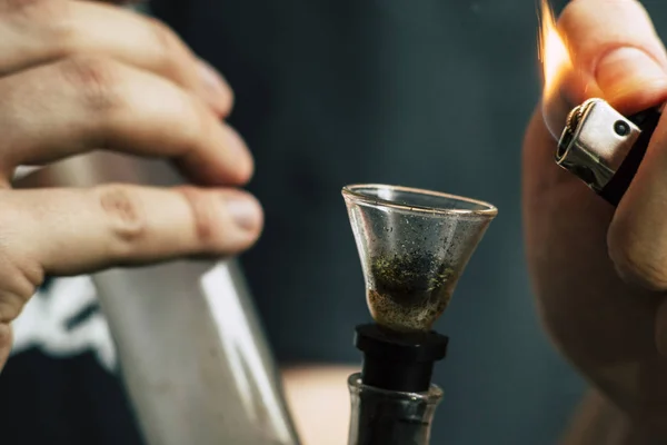 Bong-Feuerzeug für einen Mann raucht Cannabis-Unkraut, in seinen Händen. Rauch auf schwarzem Hintergrund. Konzepte des medizinischen Marihuana-Konsums und der Legalisierung von Cannabis. — Stockfoto