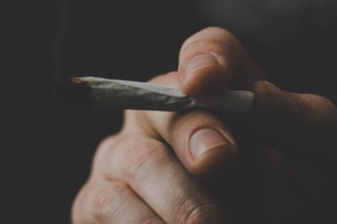 adam elinde ortak. Bir adam esrar ot çekiyor bir. Siyah bir arka plan üzerinde duman. Tıbbi esrar kullanım ve yasallaştırma esrar kavramları.
