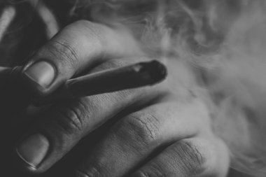 adam elinde ortak. Bir adam esrar ot çekiyor bir. Siyah bir arka plan üzerinde duman. Tıbbi esrar kullanım ve yasallaştırma esrar kavramları. Siyah ve beyaz