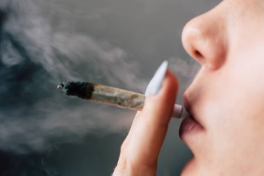 Esrar ot, onun eller A kadın ortak bir çekiyor. Siyah bir arka plan üzerinde duman. Tıbbi esrar kullanım ve yasallaştırma esrar kavramları.