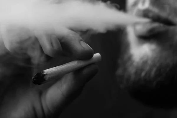 Un homme fume de l'herbe, du cannabis, un joint et un briquet dans ses mains. Fumée sur fond noir. Concepts de la consommation de marijuana médicale et de la légalisation du cannabis.Noir et blanc — Photo