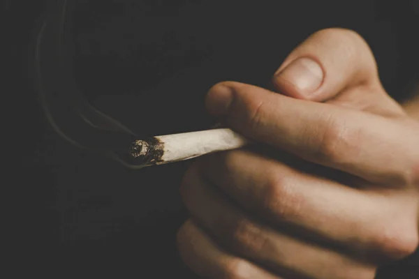 Сустав в руке человека. Мужчина курит марихуану, а. Дым на черном фоне. Концепции использования медицинской марихуаны и легализации марихуаны . — стоковое фото