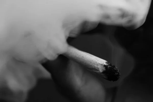 Un homme fume de l'herbe de cannabis, un joint et un briquet dans ses mains. Fumée sur fond noir. Concepts de la consommation de marijuana médicale et de la légalisation du cannabis.Noir et blanc — Photo