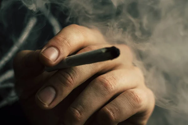 大麻杂草, 在他手中的一个男人抽烟的联合。黑色背景下的烟雾。医用大麻的概念与大麻合法化. — 图库照片