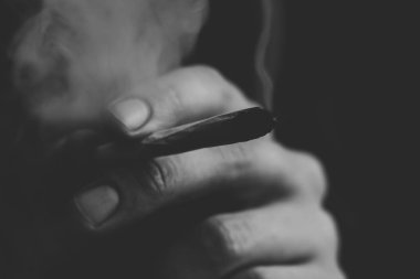 Bir adam sigara esrar esrar, esrar ve çakmak elinde. Siyah bir arka plan üzerinde duman. Tıbbi esrar kullanım ve yasallaştırma esrar kavramları. Siyah ve beyaz