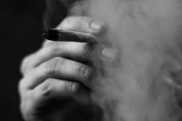 Cannabis weed A man smokes, a joint and a lighter in his hands. Smoke on a black background. Concepts of medical marijuana use and legalization of the cannabis.Black and white — Stock Photo, Image